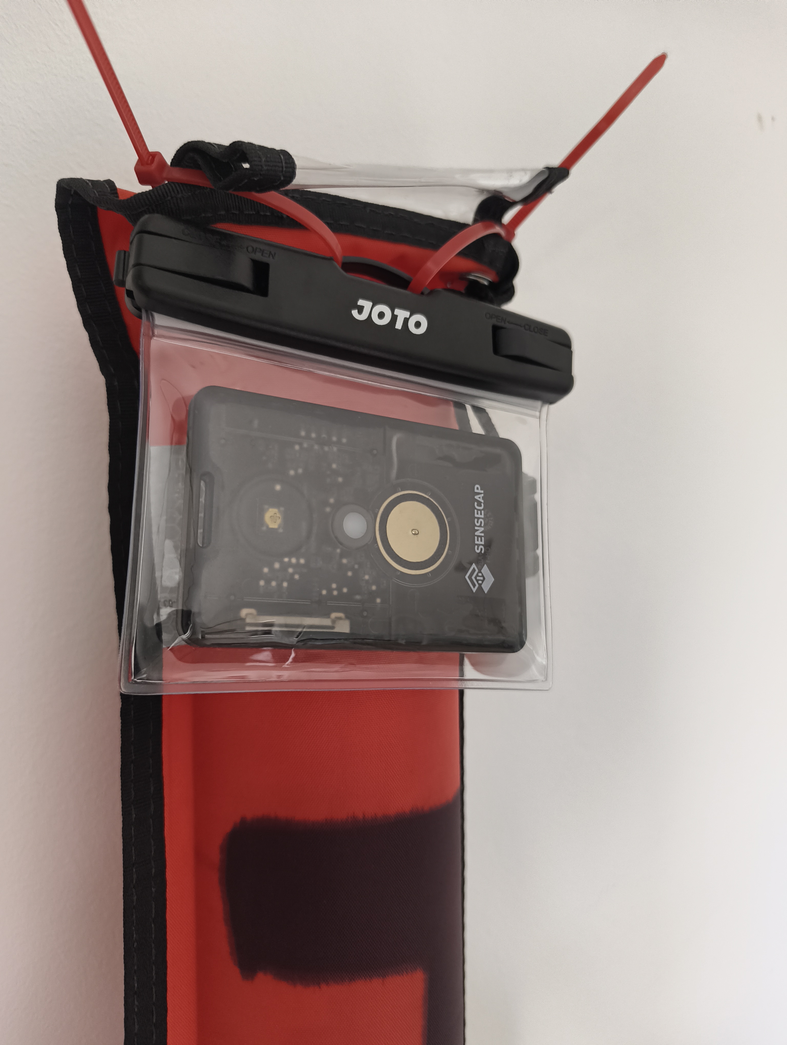 SenseCAP T1000-E inside a JOTO waterproof pouch, cable-tied to the top of a red DSMB tube
